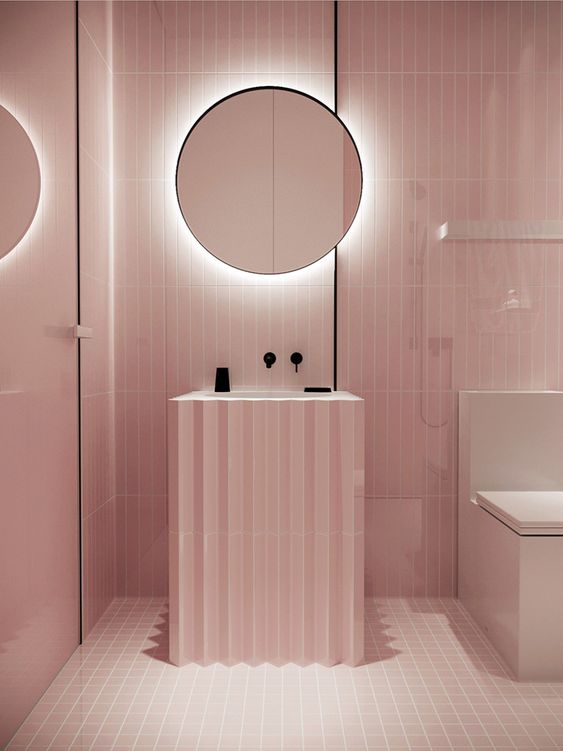 A minimalist light pink bathroom with black touches for depth and a mirror with built-in lights.