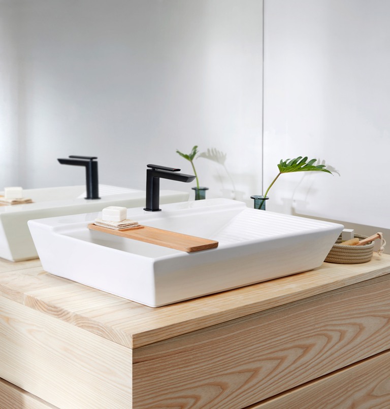 The washbasin has a geometric shape, a black matte tap and a little wooden tray.