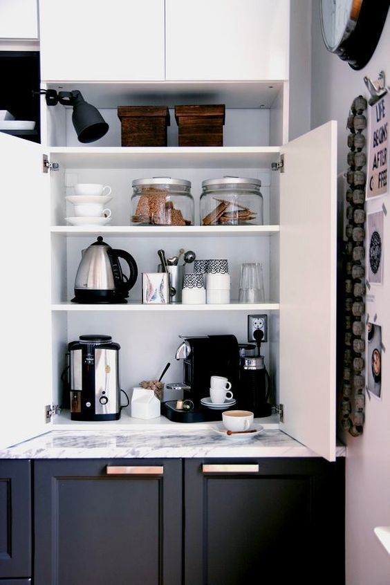 A home tea and coffee bar with all the necessary appliances and various cups and cookies hidden inside a kitchen cabinet.