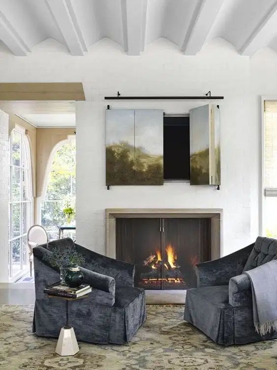 A cozy sitting nook with a real fireplace with a metal screen and a TV hidden behind an artwork that can be folded to watch TV.
