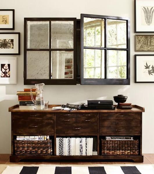 A dark-stained storage unit with baskets and a TV hidden behind mirror framed doors not to break the harmony of the space.
