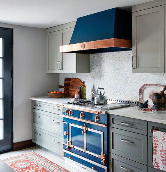 A deep blue kitchen stove with a copper touch and a matching hood in a grey kitchen.