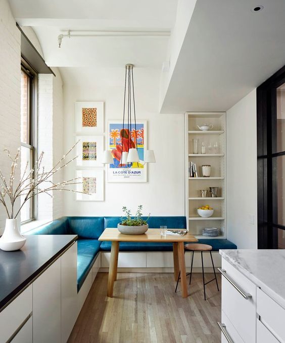 A colorful eat-in kitchen nook with an L-shaped teal bench and a wooden table doesn't take much space.