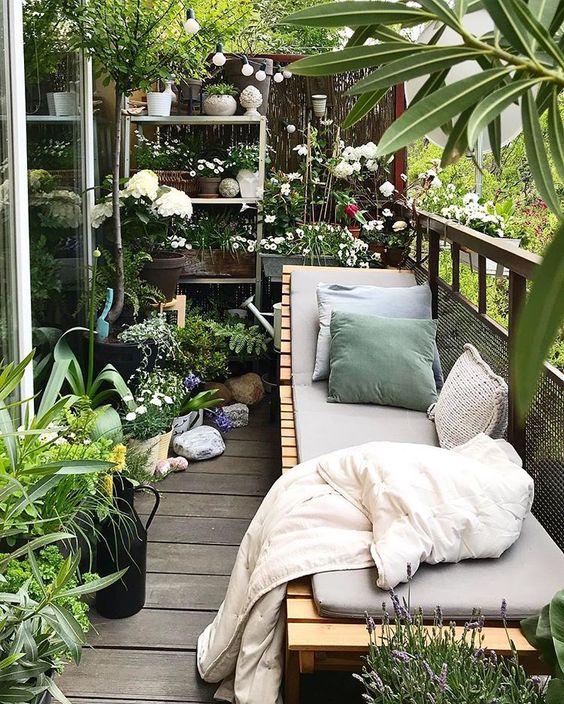 A balcony garden with potted greenery and blooms and a wooden lounger with upholstery and pillows is a gorgeous place to be.