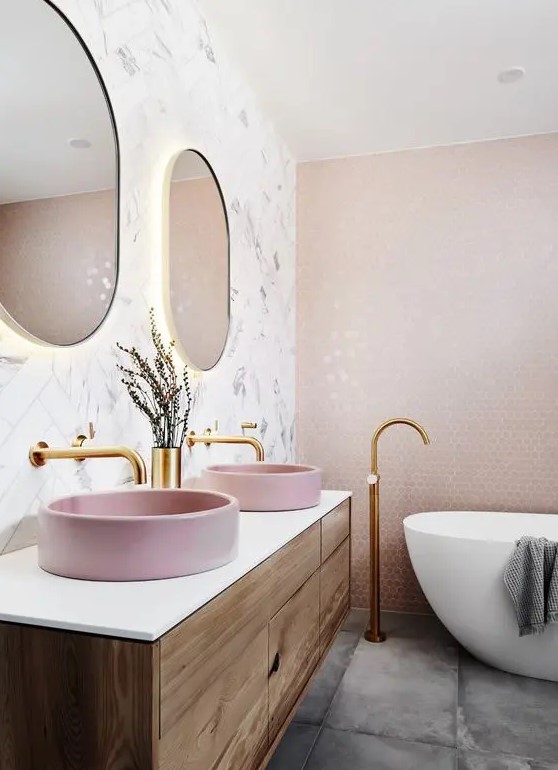 A beautiful bathroom with a marble herringbone tile wall and a pink penny one, a concrete floor and a floating vanity with pink sinks.