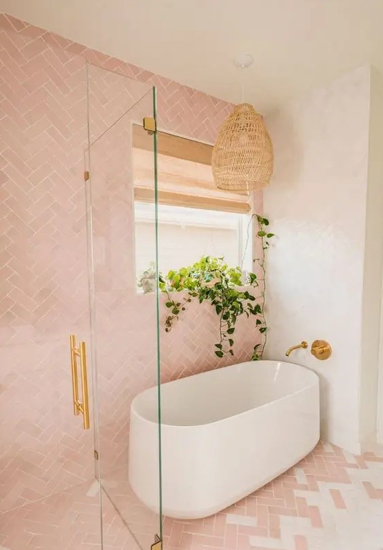 A stunning pink and white bathroom featuring elegant herringbone tiles, an oval bathtub, and gold fixtures. A woven pendant lamp adds a touch of warmth and texture to the space, creating a perfect blend of style and comfort.