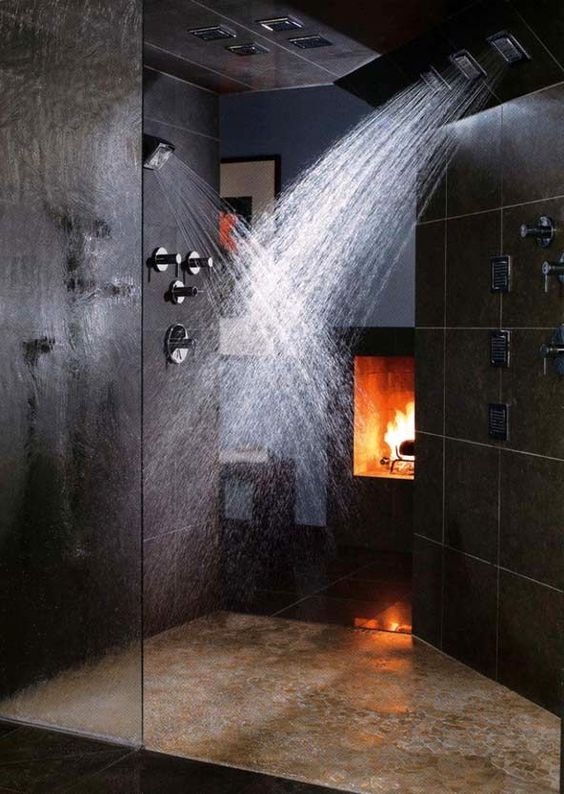 A black and dramatic shower space with stone tiles, a fireplace and rain shower heads on the walls and ceiling.