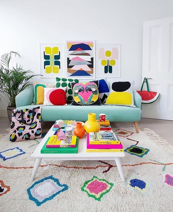 A bold summer living room with a colorful gallery wall, bright printed pillows and a rug plus bright books and vases.