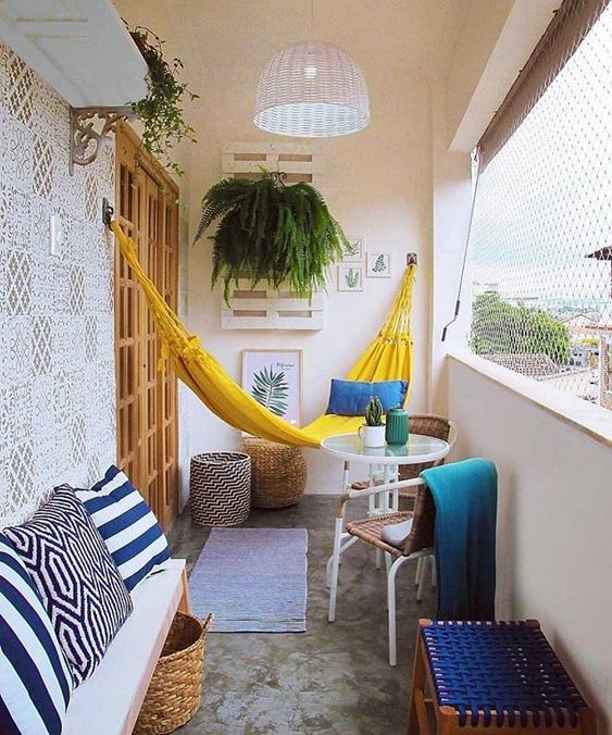 A bright and cheerful summer balcony in yellow and blue, with printed and just bright textiles, a yellow hammock and some greenery.