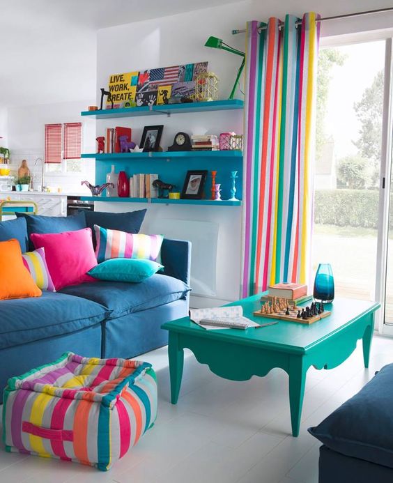 A bright living room with striped curtains, a matching ottoman, colorful pillows and some bold furniture for fun.
