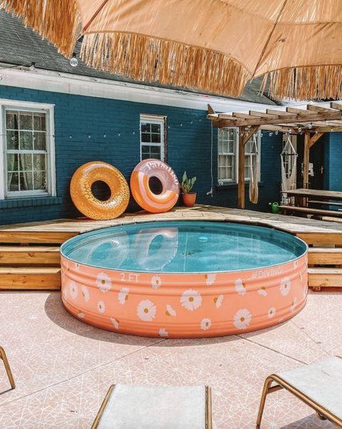 A bright outdoor space with a coral stock tank pool, a wooden deck and some floats, some umbrellas is a lovely nook.