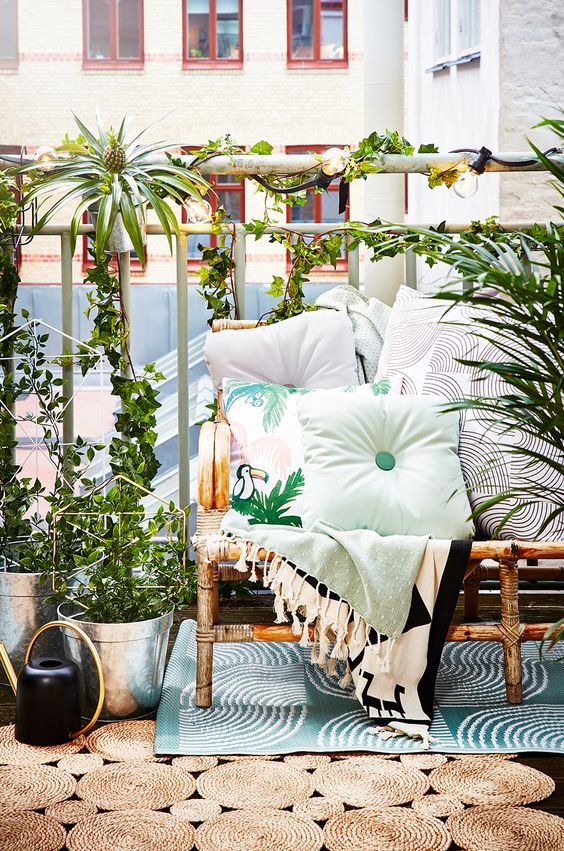 A bright summer balcony with a rattan sofa, printed textiles, potted greenery and layered rugs feels very tropical-like.