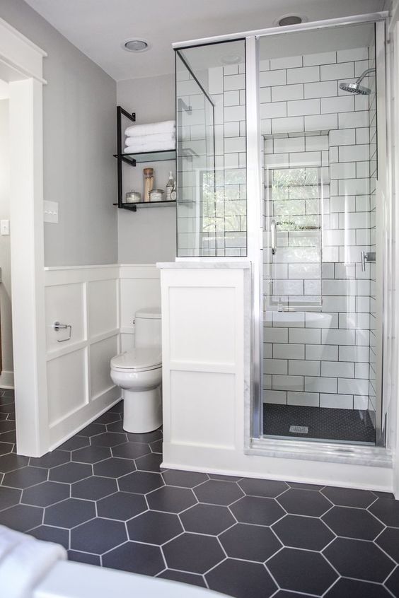 A chic bathroom with a black hex tiles floor, white subway tiles in the shower space and white paneling on the wall.
