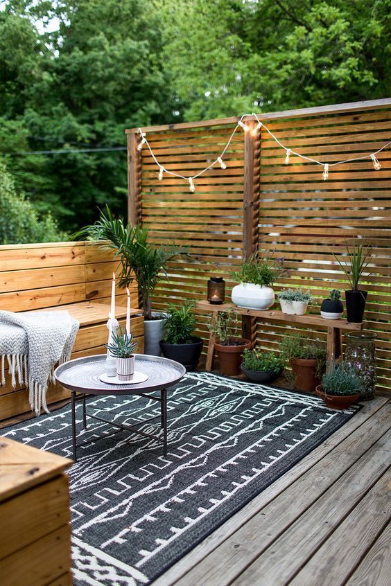 A chic monochromatic Scandinavian terrace with built-in wooden benches, lights, potted greenery and simple textiles.