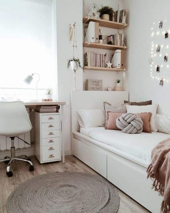 Wall-mounted shelves in this chic neutral teen room offer stylish storage above a comfy white bed with numerous pillows. The desk and white chair make a practical study area, and potted plants add a fresh, natural element to the decor.