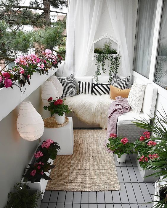 A chic yet small summer balcony in white, with sheer curtains, a jute rug, potted blooms, paper lanterns and printed textiles.