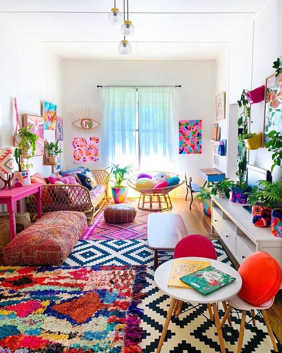 A colorful boho living room with a bright gallery wlal, colorful rugs and pillows, potted greenery and florals is summer-like.