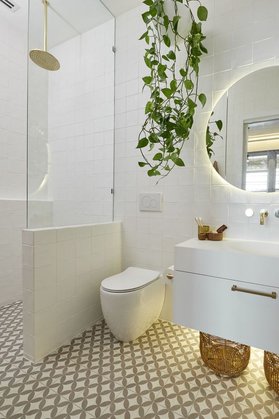 A contemporary bathroom clad with mosaic tiles, with a floating vanity, a half wall with glass to separate the shower space and a potted plant.