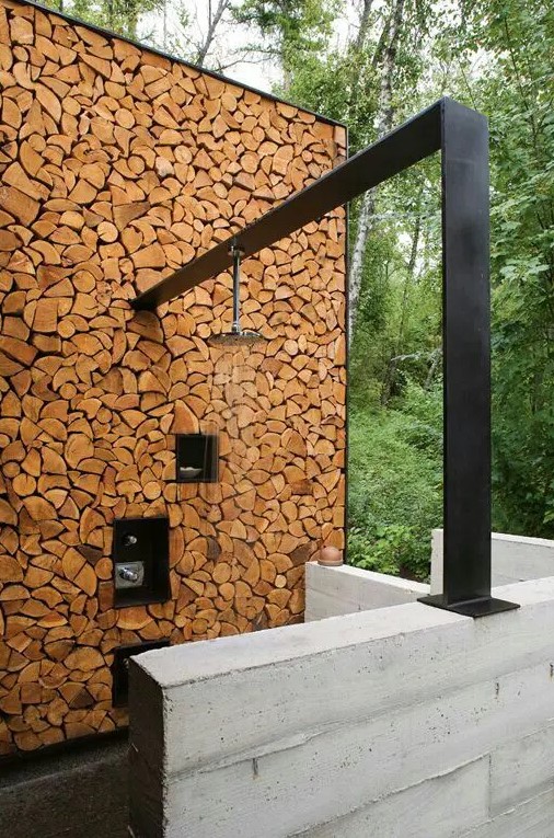 A contemporary rustic outdoor shower with a firewood wall and a dark metal panel.