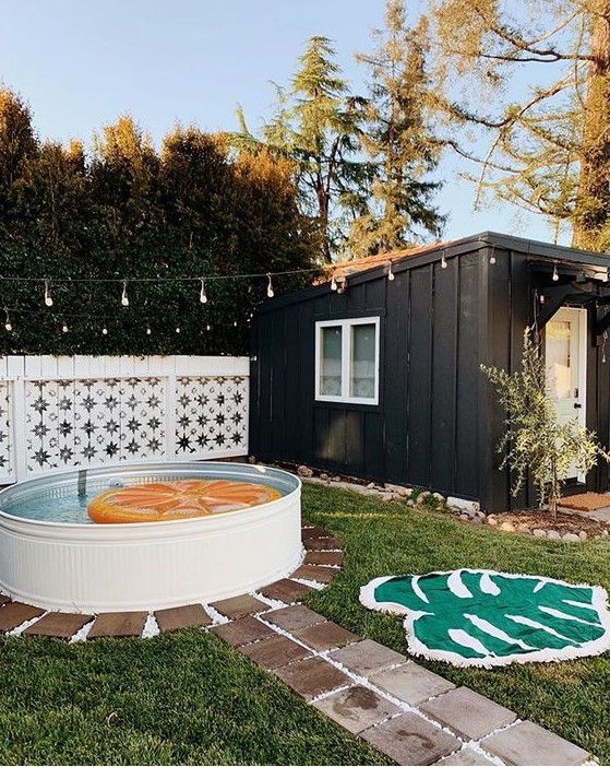 A cool backyard pool space with a stock tank pool and a bright float, a bold rug and a stone path plus lights over the space.