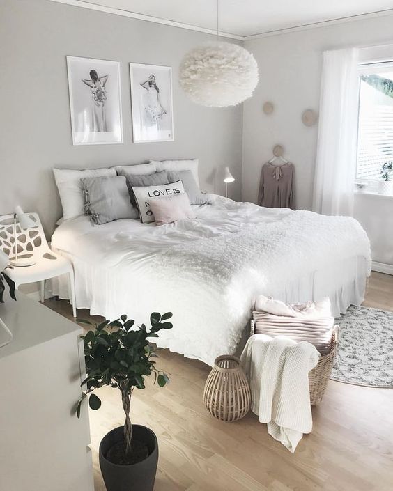 A cool neutral teen girl bedroom with a grey accent wall, a bed with neutral bedding, a white chair, a dresser, some artwork and a fluffy lamp.