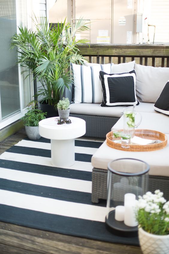A cozy monochromatic balcony with printed textiles, statement greenery and blooms, candle lanterns and wicker furniture.