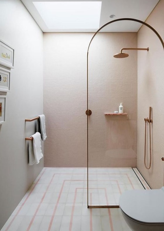 A cute contemporary bathroom with blush tiles on the walls, a patterned tile floor, brass fixtures and a brass frame divider.