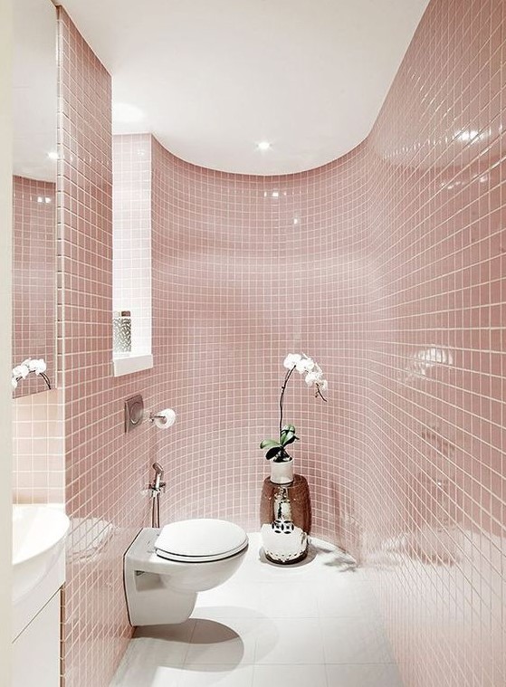 A delicate blush bathroom all clad with tiles, with a window, white appliances and a potted orchid for a touch of luxury.