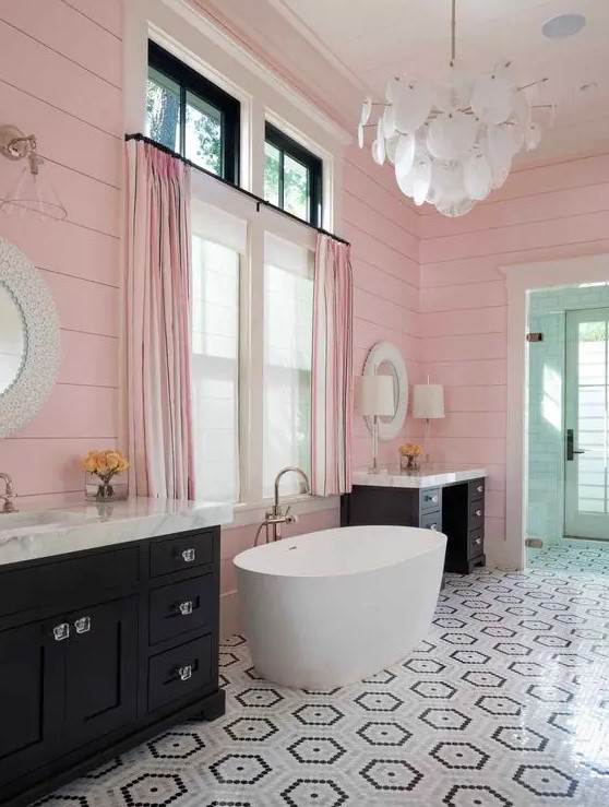 Black vanities and an oval tub stand out in this delightful bathroom with pink slatted walls. A geo tiled floor and scale chandelier add elegance. Opt for bold fixtures and unique lighting to create a captivating bathroom design.