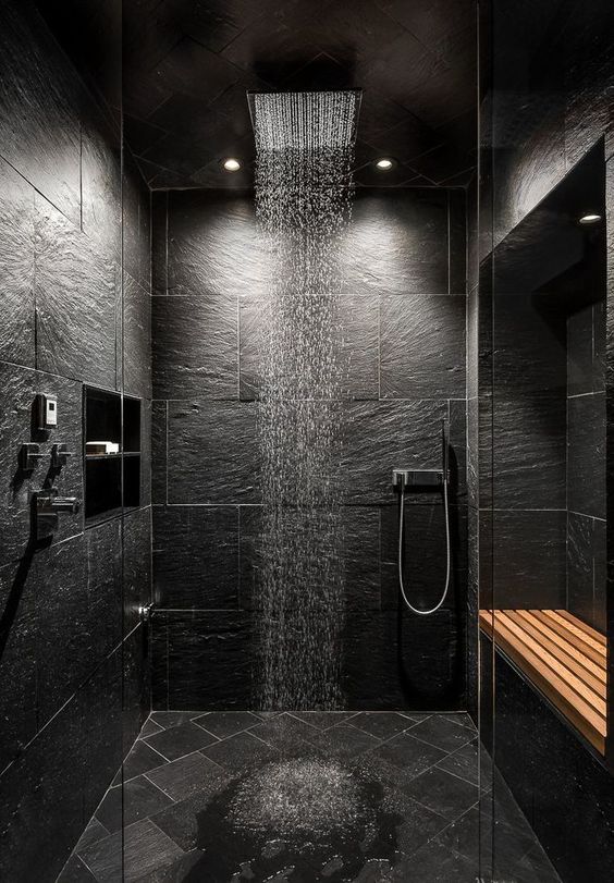 A dramatic black stone bathroom with tiles on the floor, stainless steel fixtures and a shower head plus built-in lights.