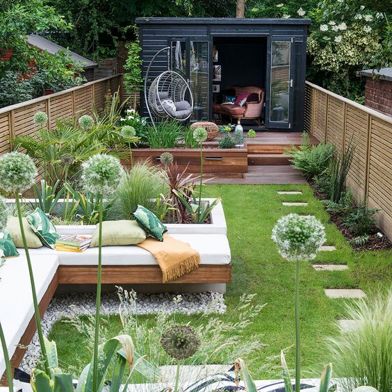 A fresh and welcoming summer terrace with a deck, a built-in bench, a lawn and some greenery and other plants.