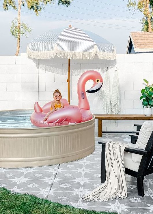 A fun and cool pool space with a stock tank pool, a flamingo float, an umbrella, a bench and a lounger is super chic.