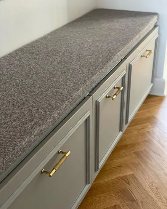 A grey storage bench built of IKEA Metod, with shaker cabinets, gold handles and a grey seat on top is stylish.