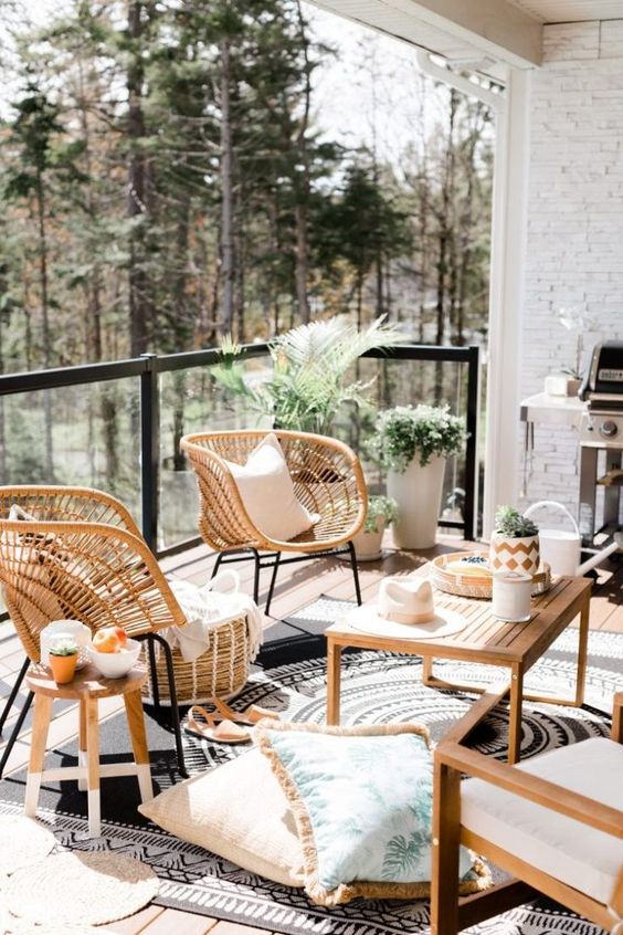 a large and welcoming balcony with wooden and wicker furniture, potted plants, a grill and some cozy textiles.