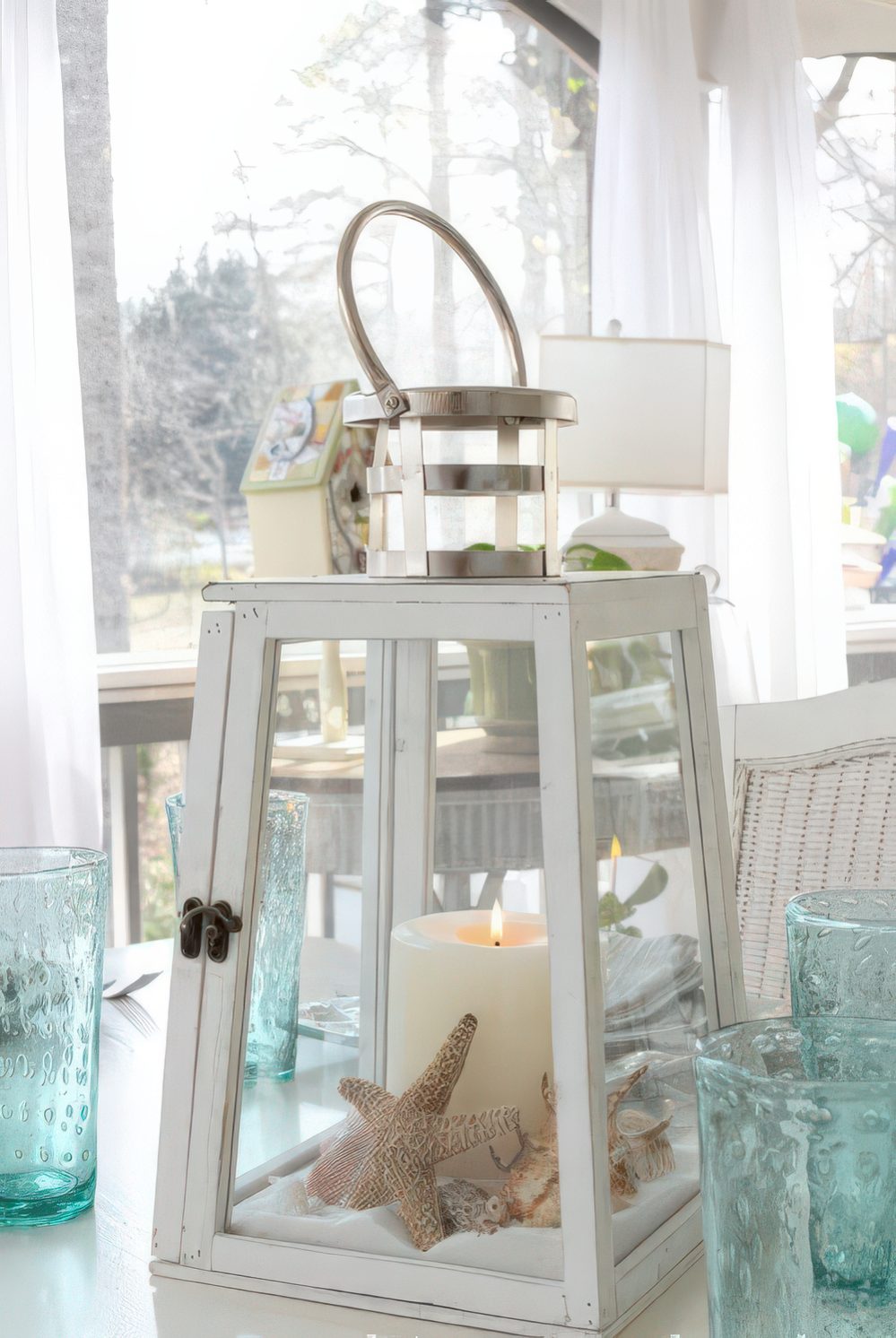 A large candle lantern with beach sand, starfish and seashells plus a large candle to decorate indoors or outdoors.