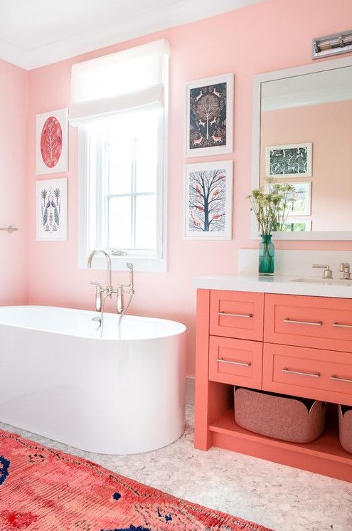 A light pink bathroom with a gallery wall, a coral vanity, a coral printed rug for a unique and very cute look.