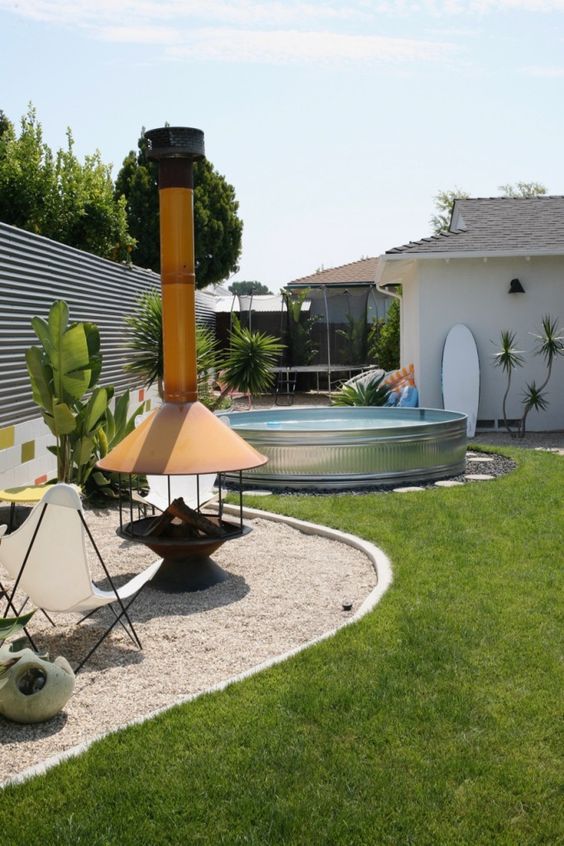 A lovely mid-century modern space with a green lawn, a fireplace and some butterfly chairs, potted plants and a stock tnak pool.