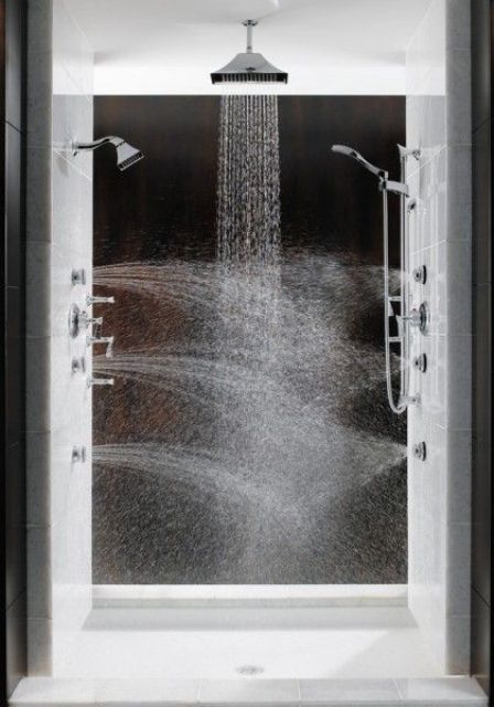 A luxurious massage shower space clad with black and white tiles, with rain shower heads on the ceiling and walls.