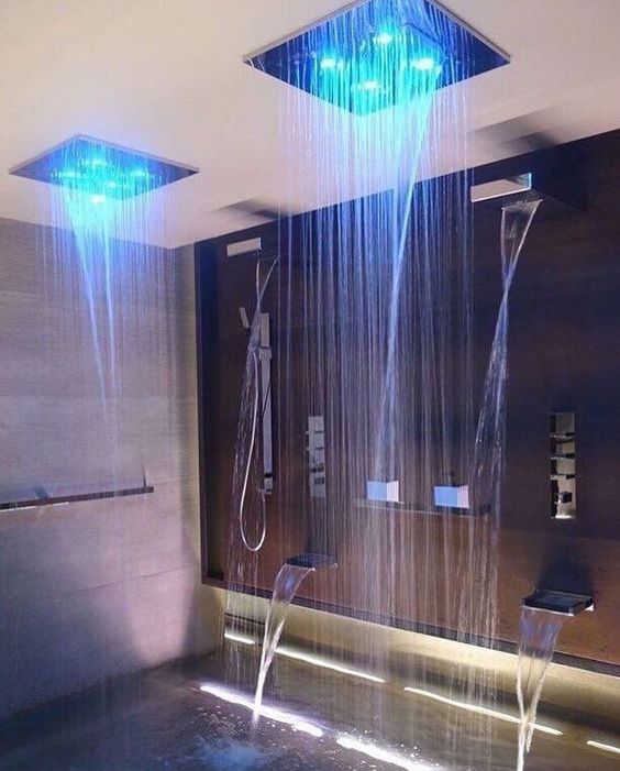 A luxurious shower space with waterfalls and waterfall and rain shower heads with regulated color lights.