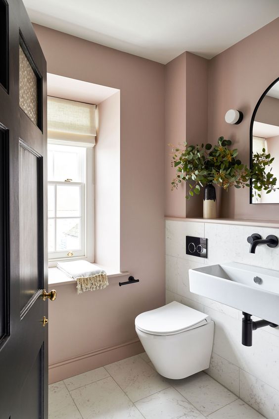 A mauve and white bathroom with white appliances, black fixtures and greenery is amazing for a modern home.