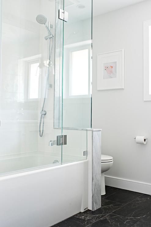 A minimalist bathroom with a black floor, a half wall that separates the toielt from the rest of the space, a shower-bathtub space.