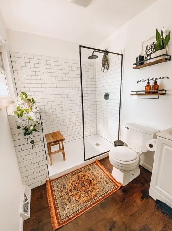 A modern farmhouse bathroom with white subway tiles, a wooden floor, white furniture, potted greenery and a boho rug.