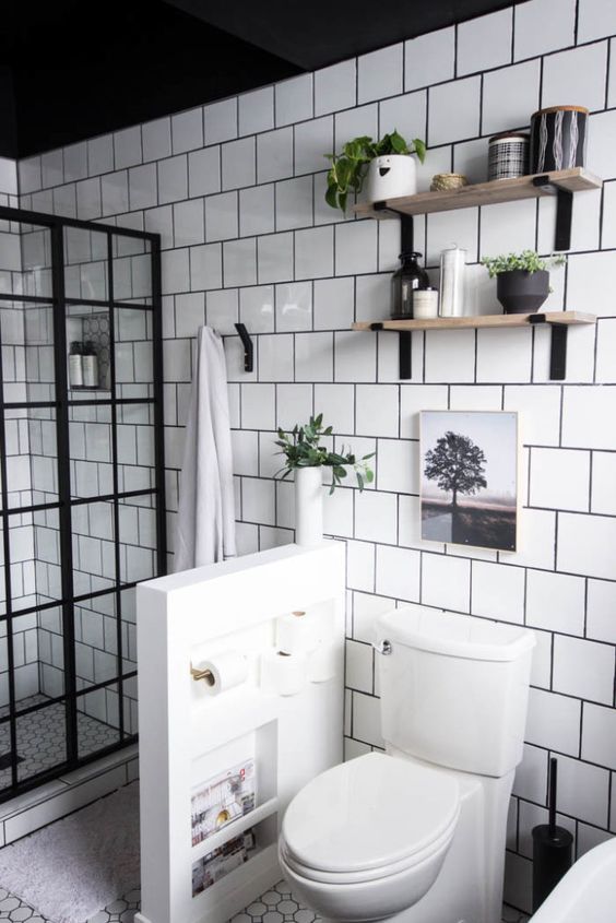 A modern neutral bathroom clad with white square tiles, with a French glass shower space, a pony wall to separate the toilet.