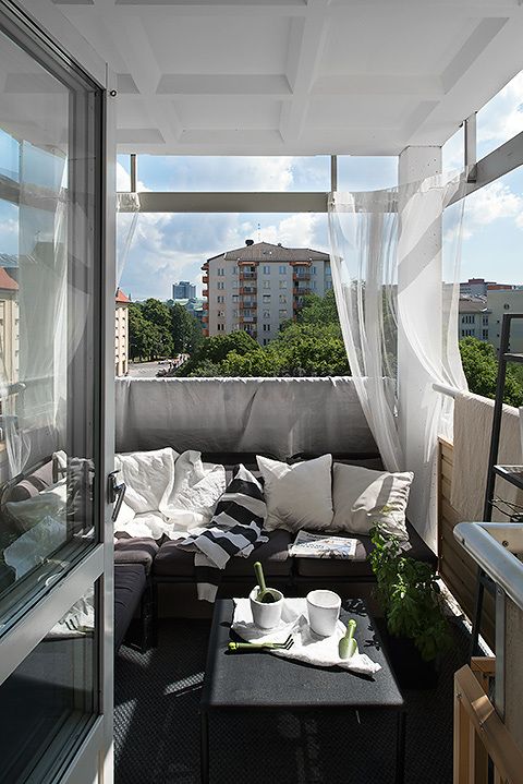 A monochromatic balcony with dark furniture, printed textiles, sheer curtains and potted greenery.