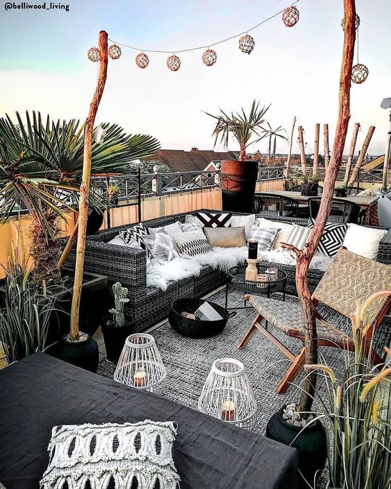 A monochromatic summer terrace with black furniture, black and white textiles, candle lanterns and potted greenery and trees.