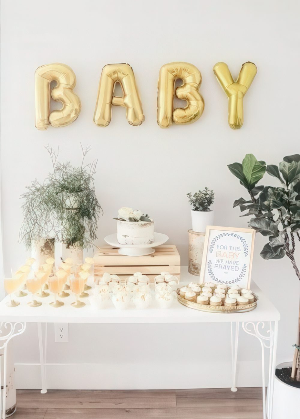 A neutral and gold baby shower dessert table with gold balloons, greenery arrangements and neutral desserts.