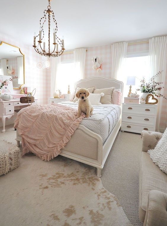 A neutral and lovely teen girl's bedroom with plaid wallpaper, a white bed with neutral bedding, white dressers, a blush vanity and a large mirror, a sofa.