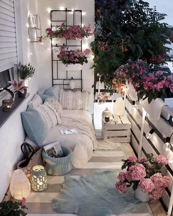 A neutral and pastel balcony with boho textiles, candle lanterns, potted greenery and lights.