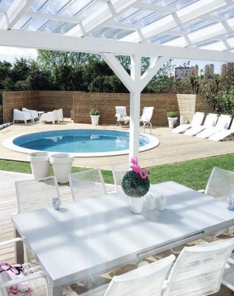 A neutral contemporary space with loungers and white garden furniture and a round pool clad in white, too.