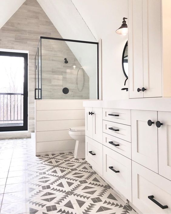 A neutral farmhouse bathroom with mosaic tiles, planked walls and cabinets, a shower space with a half wall.